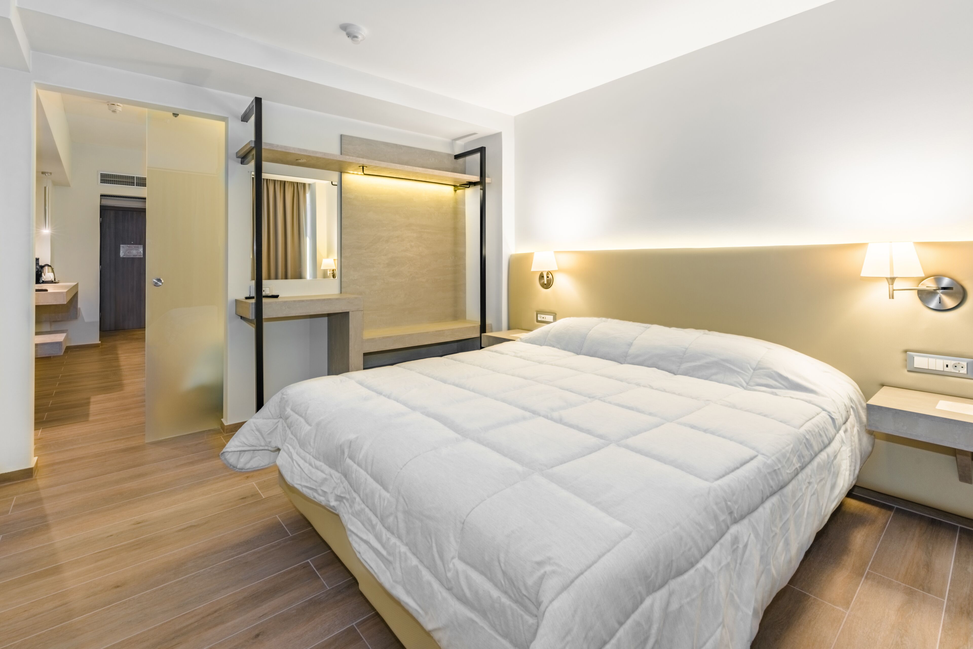Una habitación de hotel moderna con una cama grande, un tocador con espejo y un baño independiente.