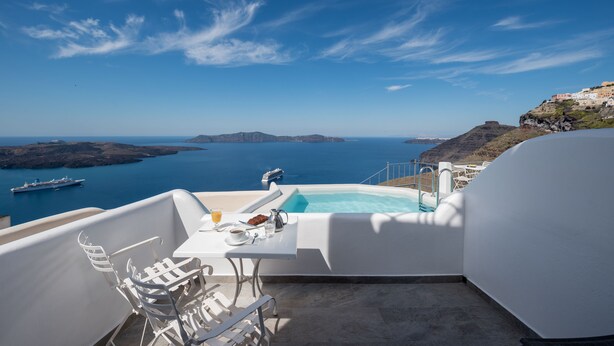 A balcony with a pool, white furniture, and a table with breakfast items. - Villa Renos (Santorini)