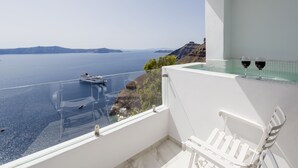 A balcony with a clear view of the sea and a yacht. There is a white chair and two wine glasses on the balcony. - Villa Renos (Santorini)