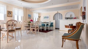 A dining area with a white table and chairs, a red rug, and a decorative mirror above the fireplace. - Villa Renos (Santorini)