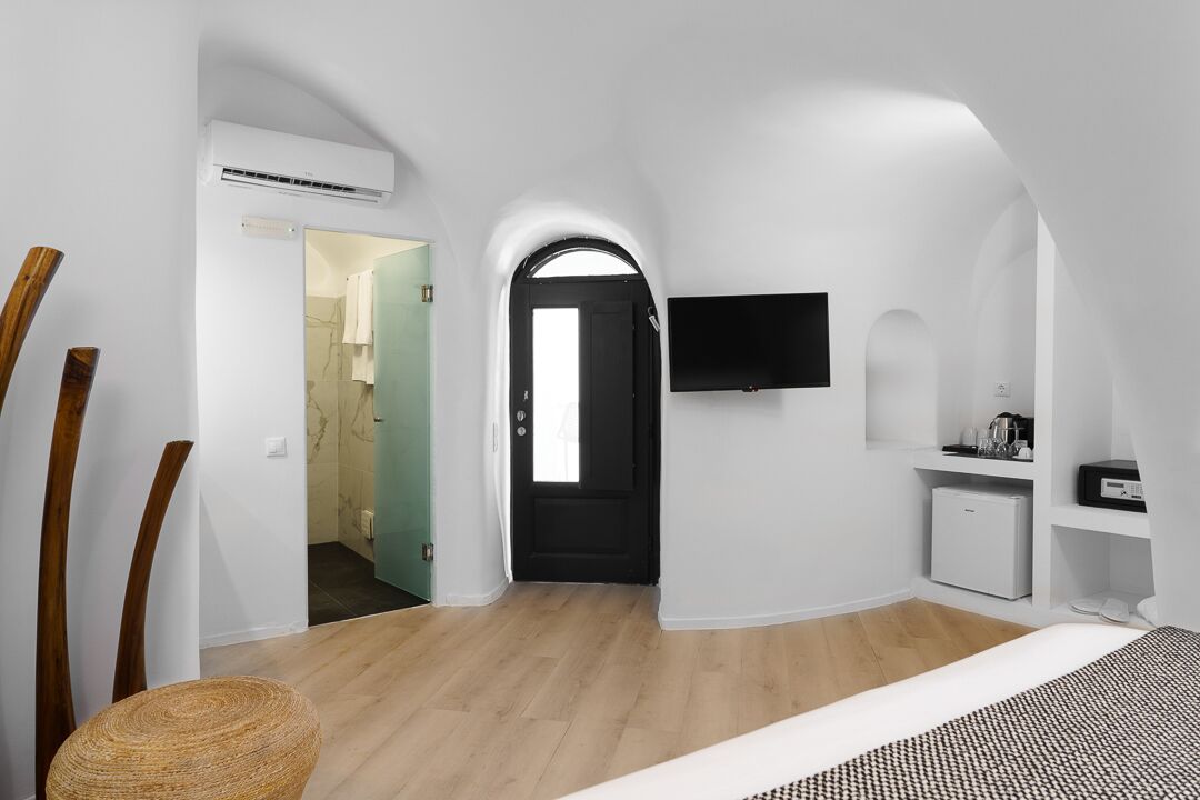 Ein modernes, minimalistisches Zimmer mit Holzboden, einer schwarzen Tür, einem Wand-Fernseher und einem kleinen, weißen Schrank.