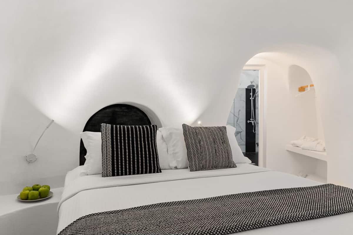 Quarto moderno com cama, almofadas, mesa de cabeceira com maçãs e vista para um banheiro.