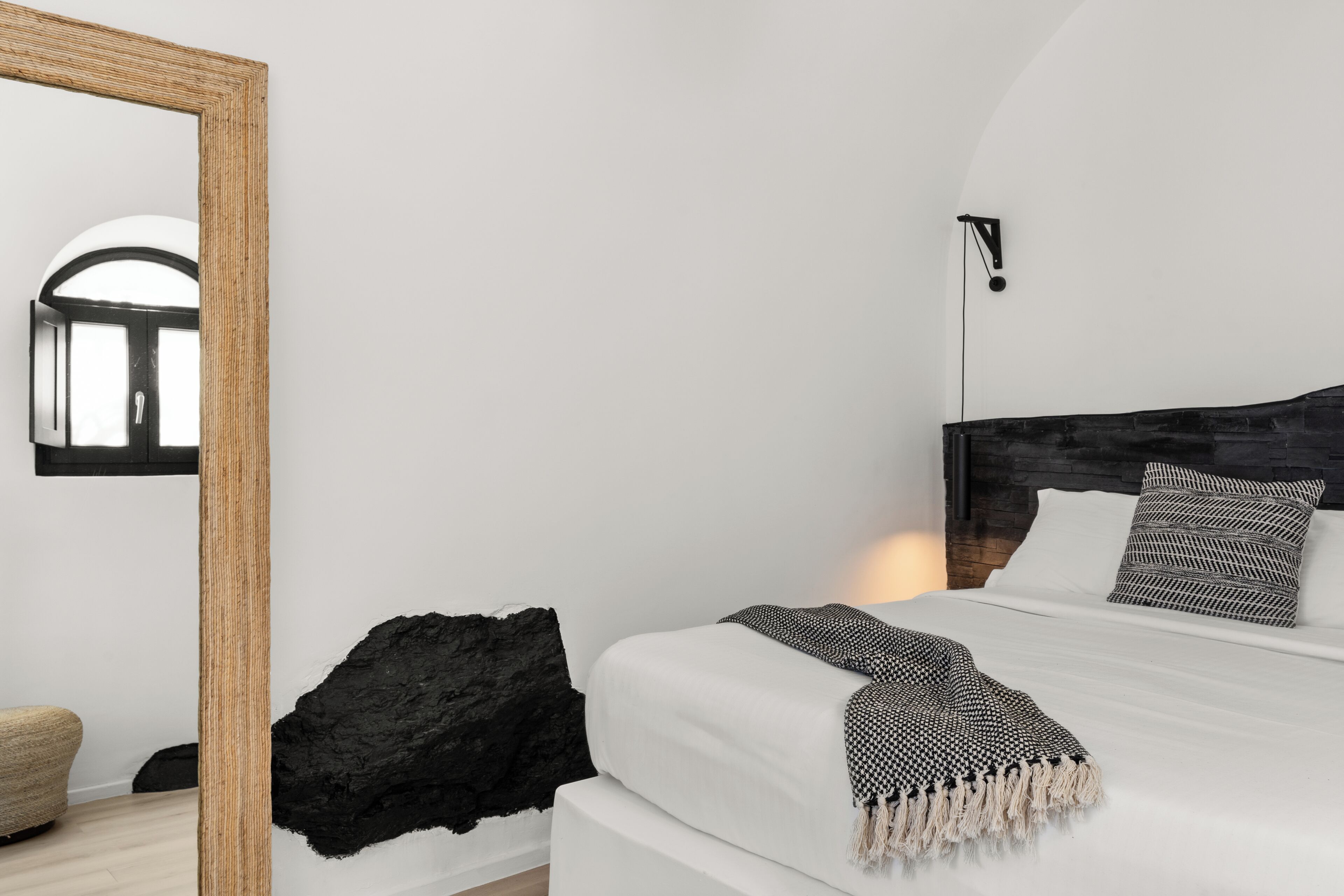 A bedroom with a large mirror, a bed with white bedding, a black headboard, and a black rock decoration.