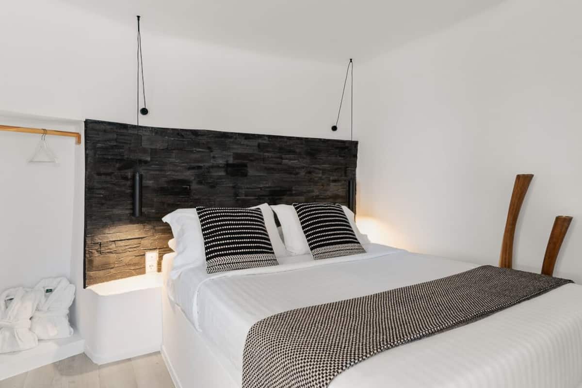 Um quarto moderno com uma cama grande, cabeceira com design texturizado, mesas de cabeceira e luminária suspensa.