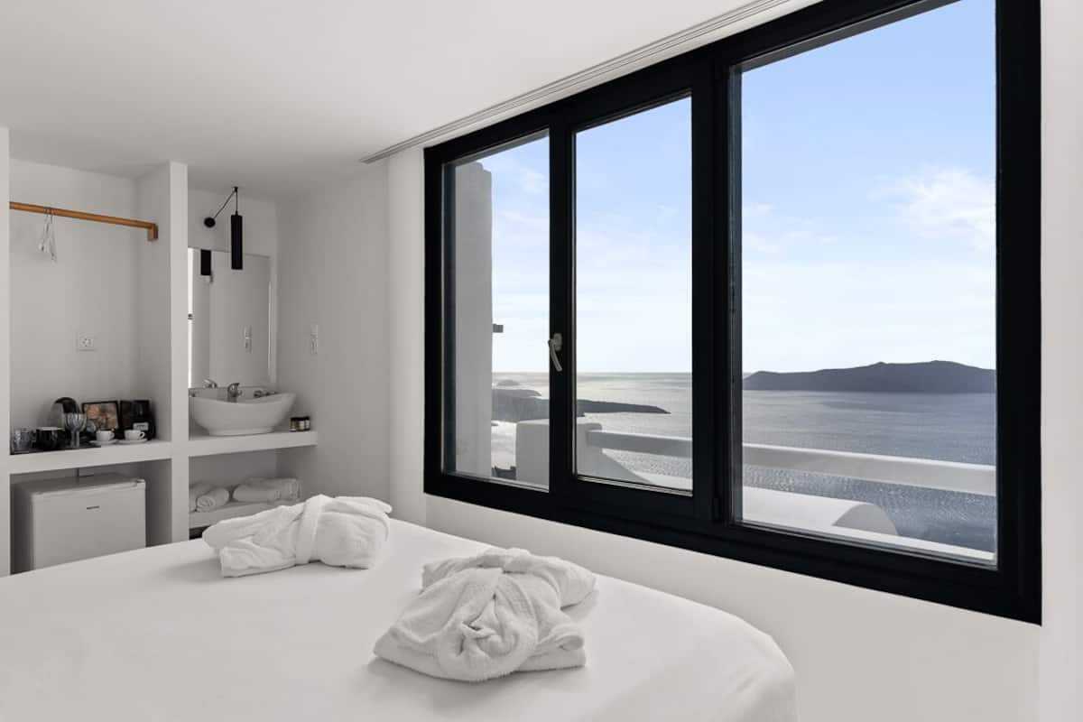 Quarto moderno com janela ampla, cama branca e pia embutida.