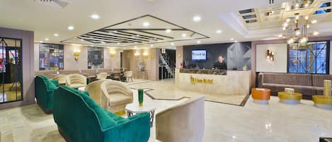 Un vestíbulo de hotel con áreas de descanso, una recepción y una escalera.