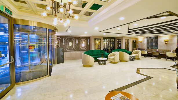 Un hall d’hôtel avec un canapé vert, plusieurs fauteuils, un comptoir d’accueil et une entrée en verre.