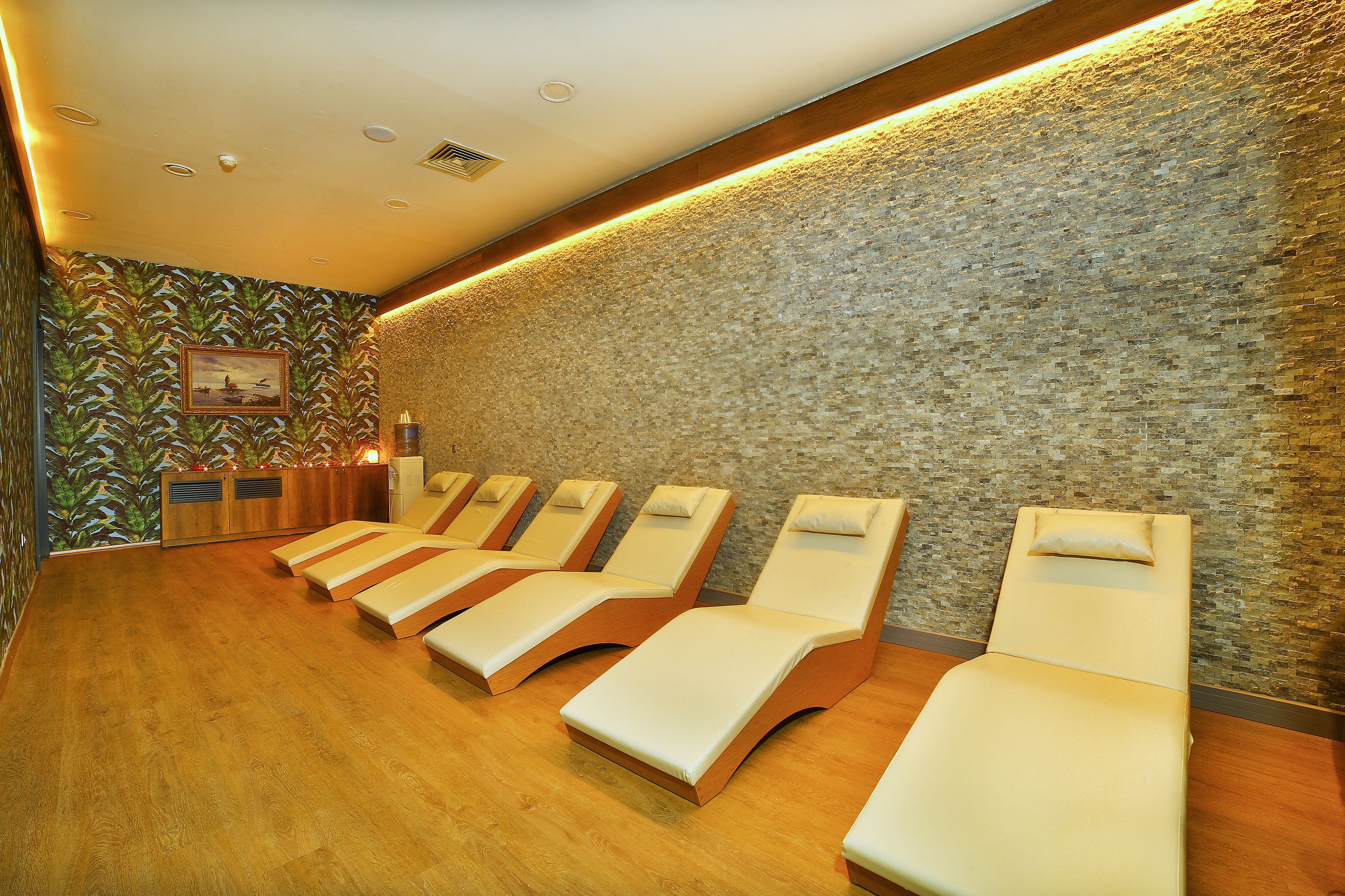 A room with wooden flooring, a stone wall, and multiple sunbeds.