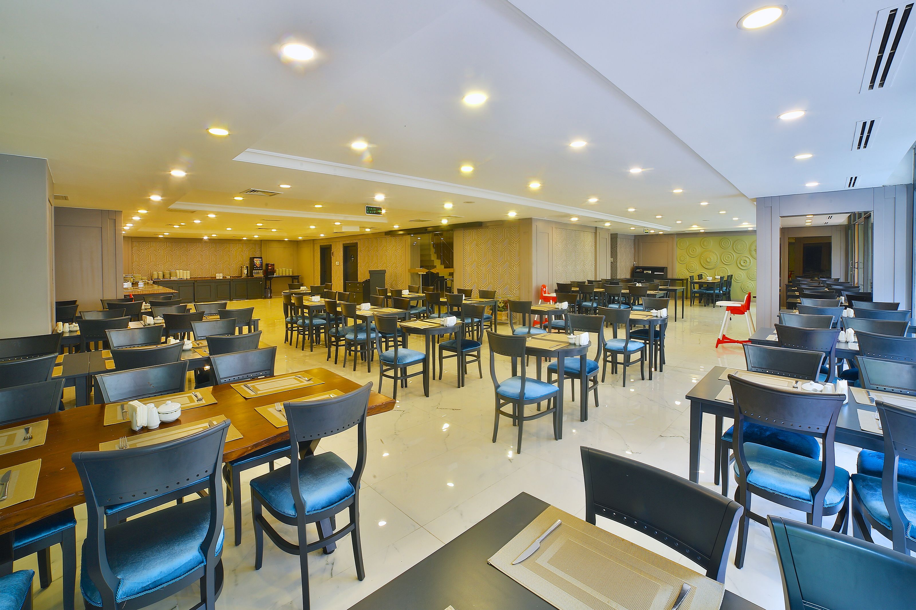 Un comedor amplio con varias mesas y sillas, una cocina al fondo, y un ambiente limpio y bien iluminado.