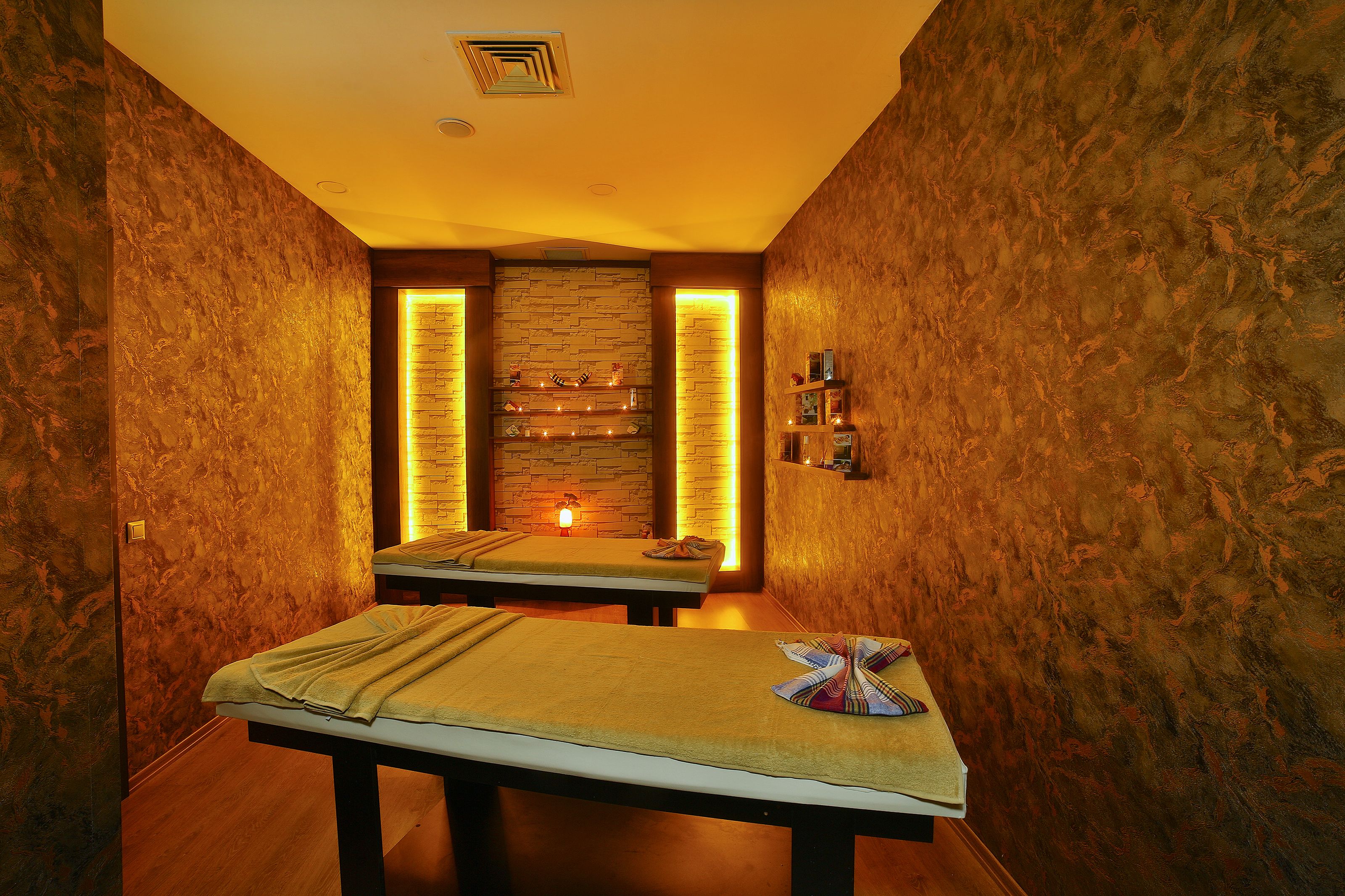 Une salle de spa équipée de deux tables de massage, d’un mur en pierre et d’une petite étagère où sont disposés divers objets.