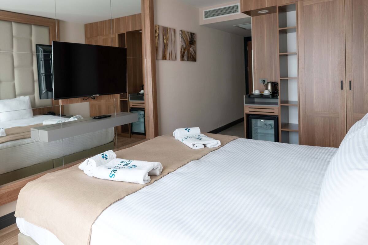 Quarto de hotel com uma cama grande, televisão, minibar e armário.