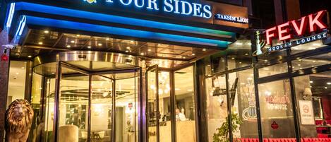 A hotel entrance with a glass door, a lion statue outside, and signs for 'Four Sides' and 'FevK Hookah Lounge'.