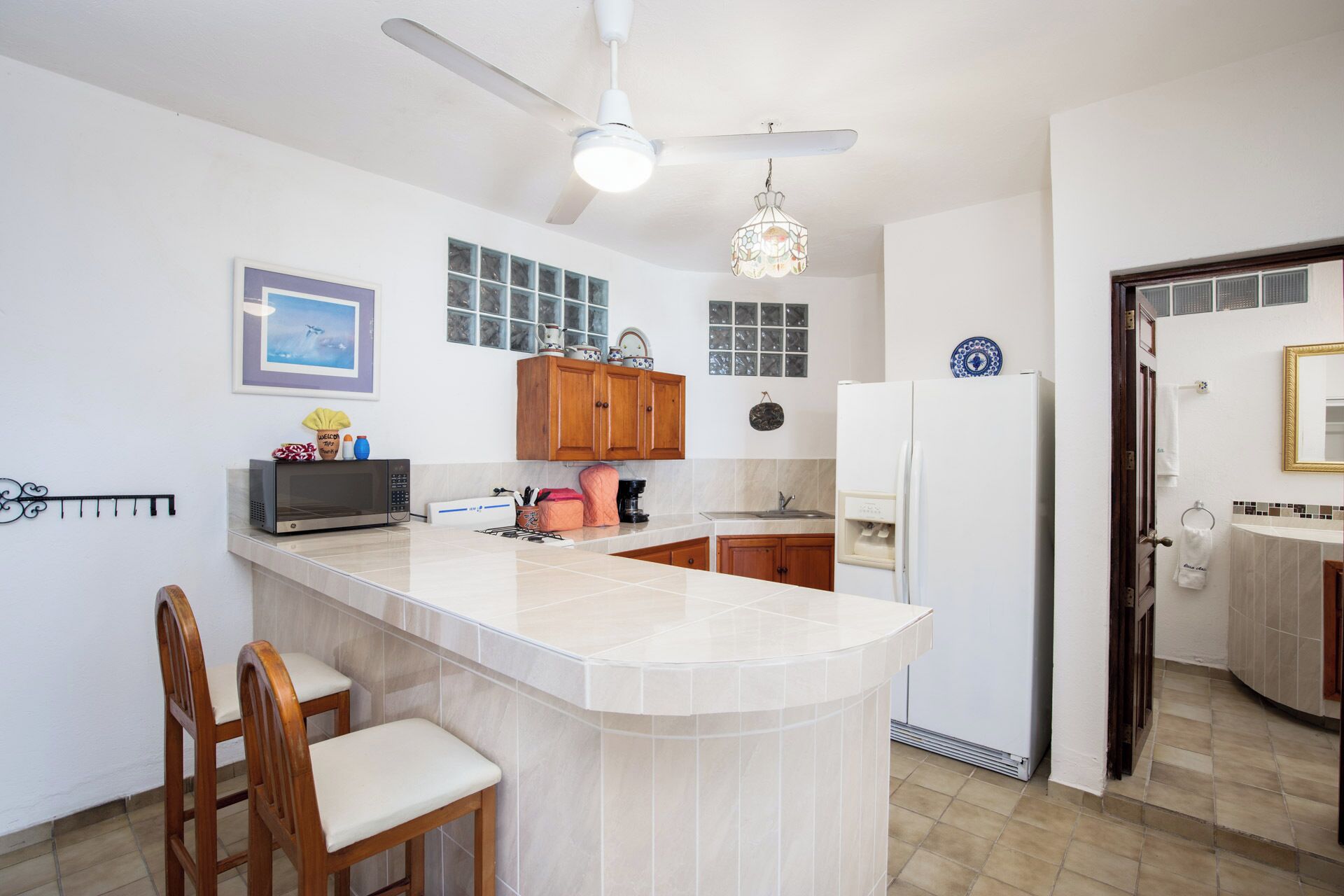 A kitchen with a central island, wooden chairs, a ceiling fan, and a refrigerator.