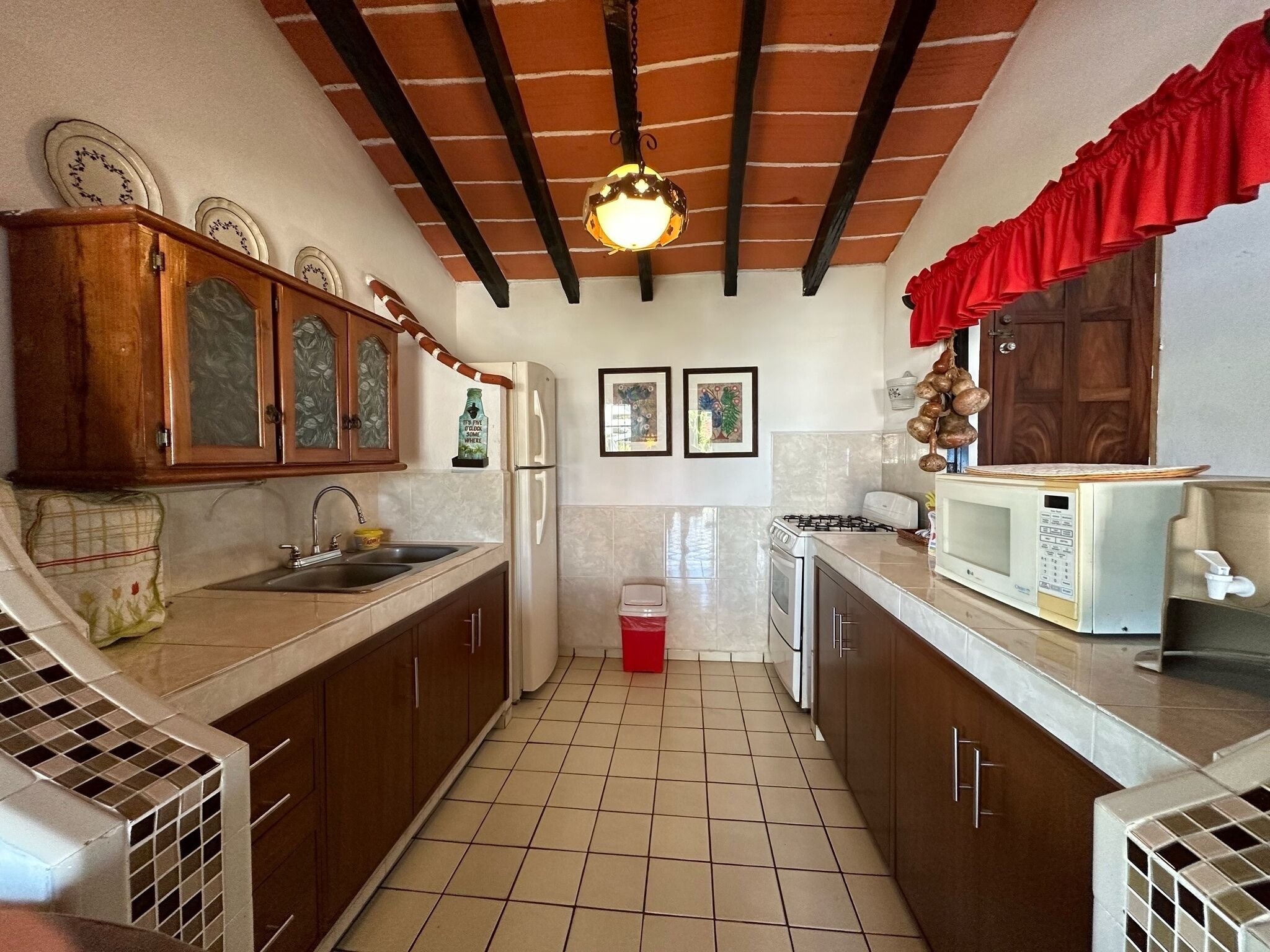 A compact kitchen with a tiled floor, wooden cabinets, a refrigerator, a stove, and a microwave.
