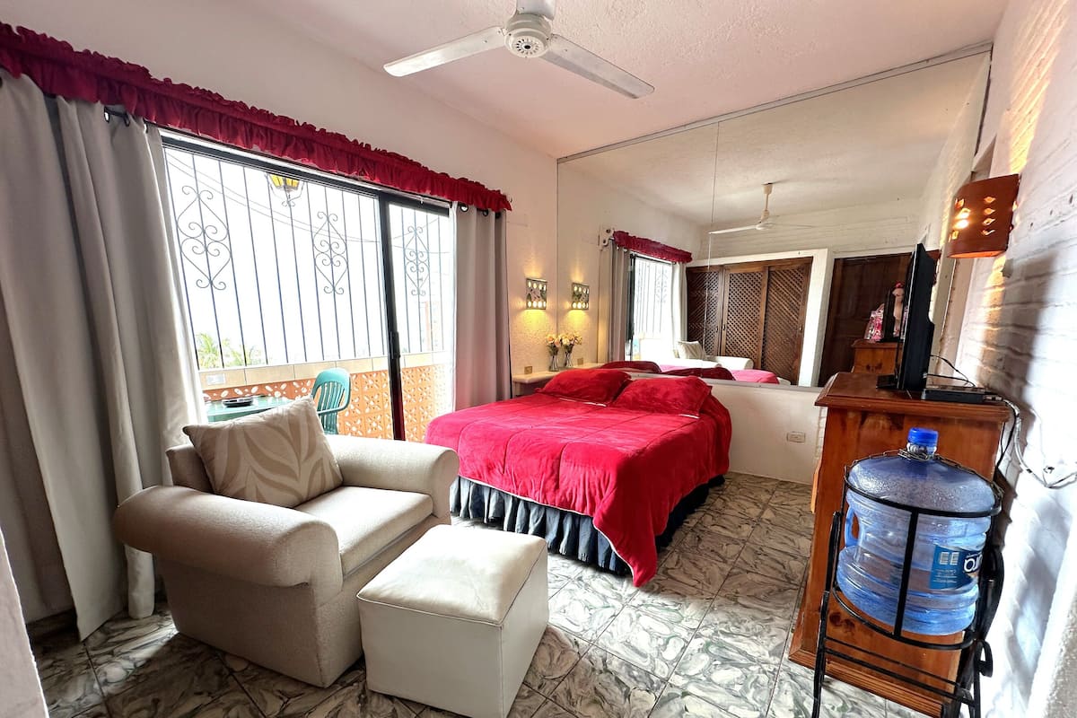 A hotel room with a bed, a sofa, a chair, a water dispenser, and a balcony with a view.