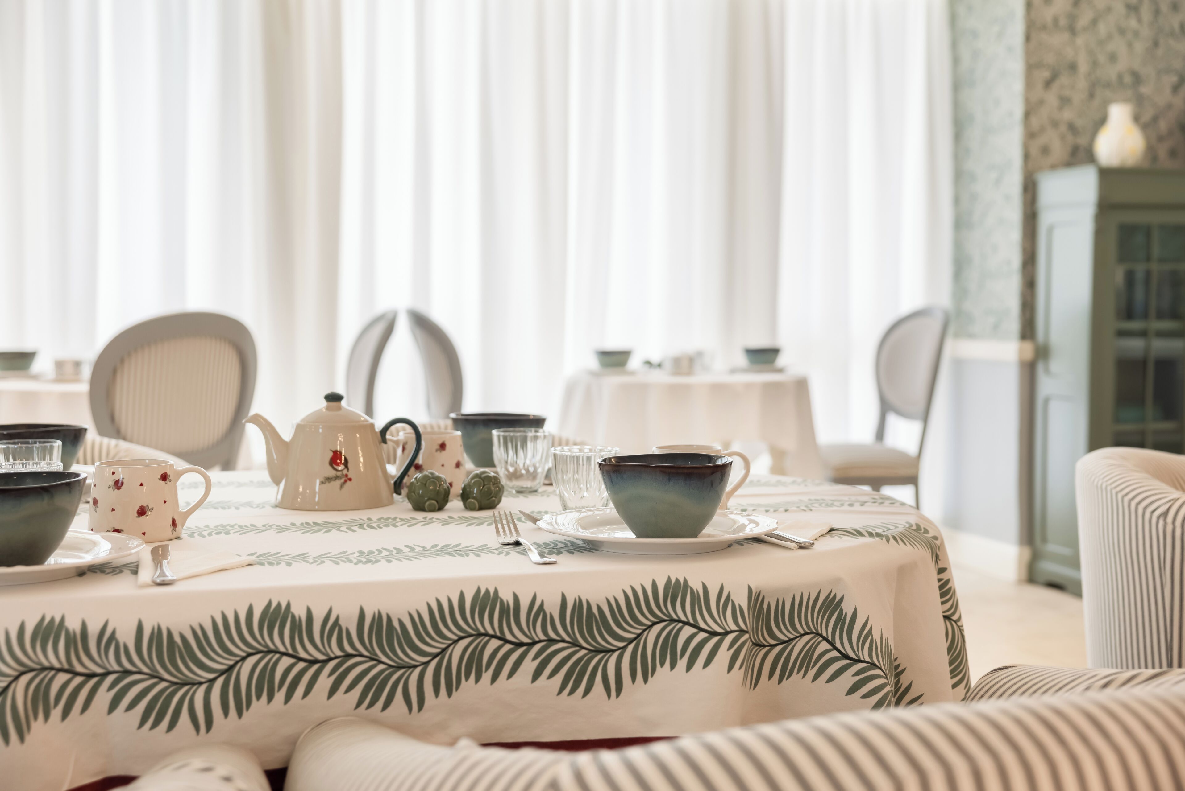 Een eettafel gedekt met theekopjes, een theepot en een tafelkleed met bloemenmotief.