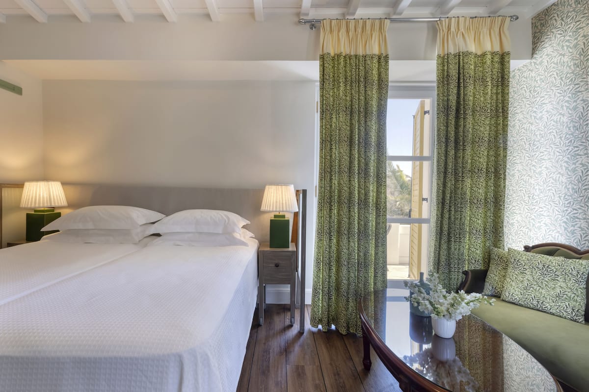A hotel room with a bed, two bedside tables with lamps, a sofa, and a window with curtains.