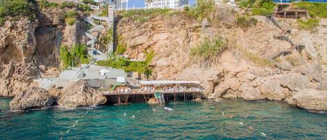 Un hotel junto a la costa, con un acantilado rocoso, un muelle y una zona de piscina.