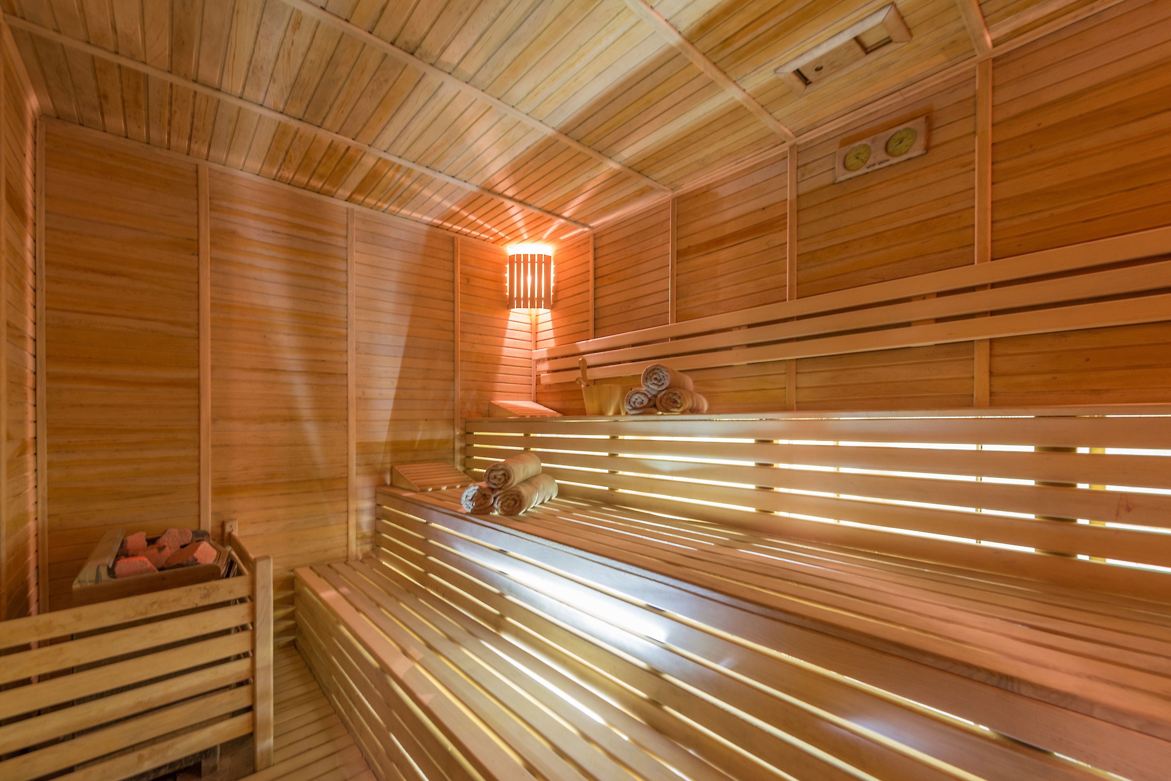 Eine Sauna mit Holzbänken, einer Bank mit Handtuch und einer Holzwand mit einer Uhr.