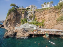 Um hotel à beira-mar com um penhasco rochoso, uma área de natação e um terraço com espreguiçadeiras.