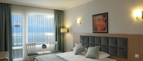 A hotel room with a large bed, a desk, a chair, and a window with curtains.