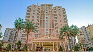 Un hotel moderno de gran altura con entrada central, varios balcones y palmeras.