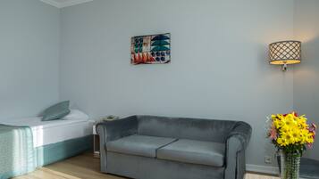A modern living room with a grey sofa, a bed with a white duvet, a wall-mounted lamp, and a painting.