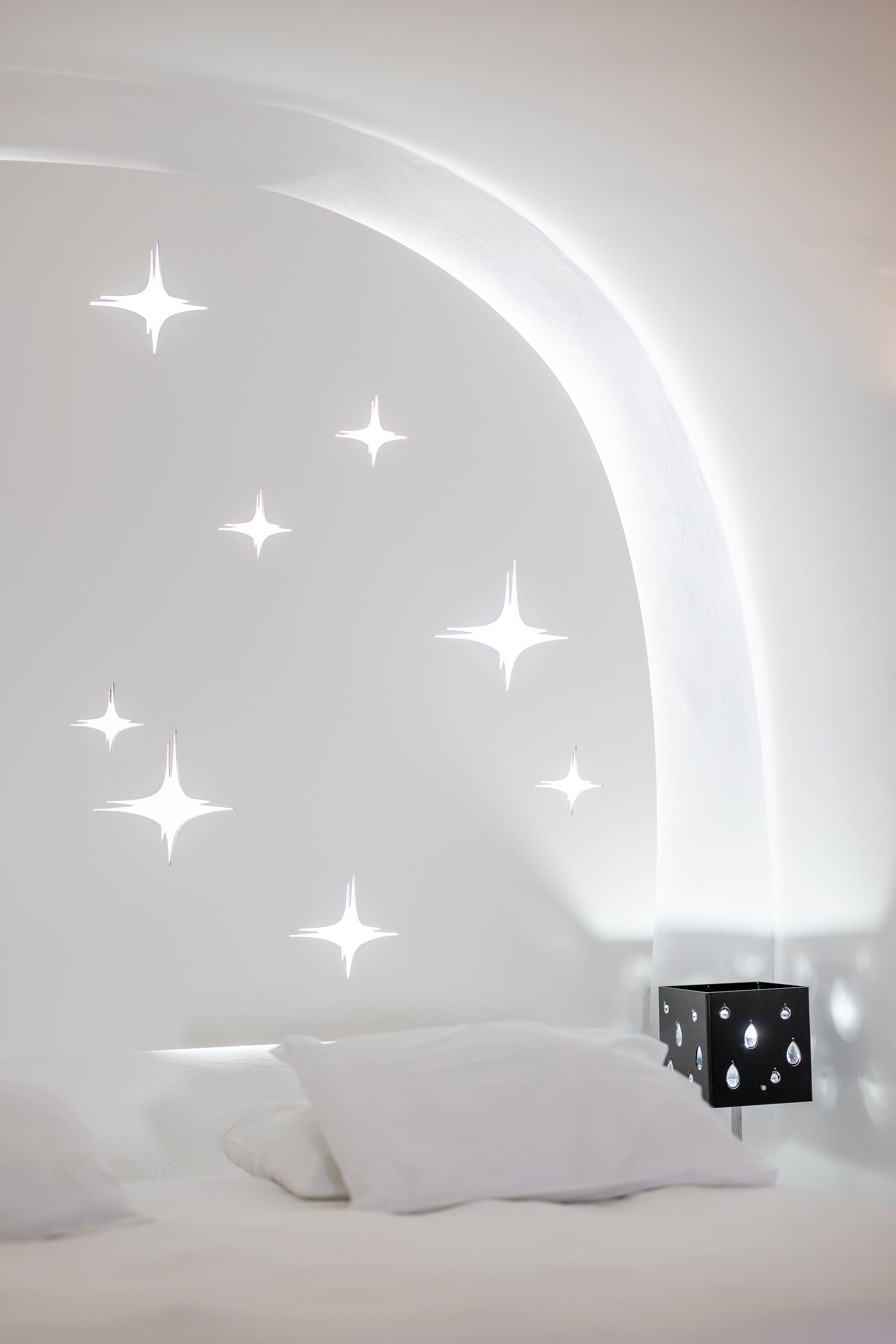 A bedroom with a curved ceiling, white bedding, and a nightstand with a black lamp.