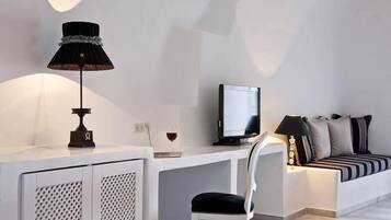 Una habitación moderna y minimalista con un escritorio blanco, una computadora, una lámpara negra, una copa de vino y un sofá con cojines a rayas.