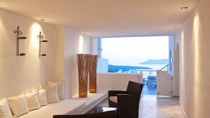 Una habitación de hotel moderna con un sofá blanco, una silla negra y un ventanal con vistas al mar.