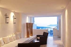 Una habitación de hotel moderna con un sofá blanco, una silla negra y un ventanal con vistas al mar.