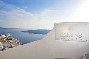 A sign for 'asteras villas' with a view of a coastal town and the sea. - Asteras Villas (Santorini)