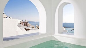 Una habitación con vista a un edificio blanco con detalles rojos, una piscina y un cielo despejado.