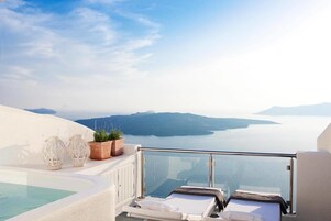 Un balcón con vistas al mar y las montañas, una piscina y dos sillas de descanso.