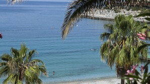 A beach with palm trees, umbrellas, and people. - Pine Bay Holiday Resort (Kusadasi)