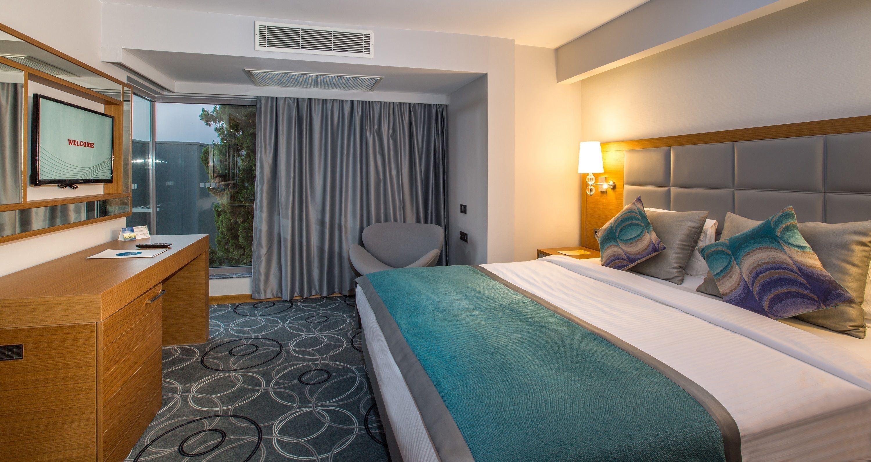 A hotel room with a bed, a desk, a chair, a TV, and a window with curtains.