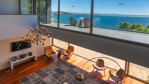 A modern living room with a large TV, comfortable seating, a stylish chandelier, and a view of the sea. - Pine Bay Holiday Resort (Kusadasi)