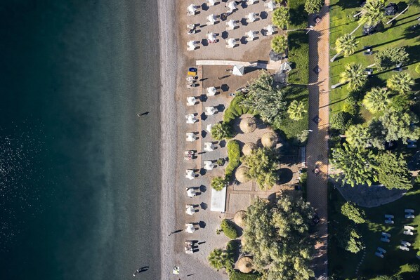 An aerial view of a beachside hotel with rows of white tents and umbrellas, palm trees, and a clear view of the ocean. - TUI BLUE Grand Azur - All inclusive (Marmaris)