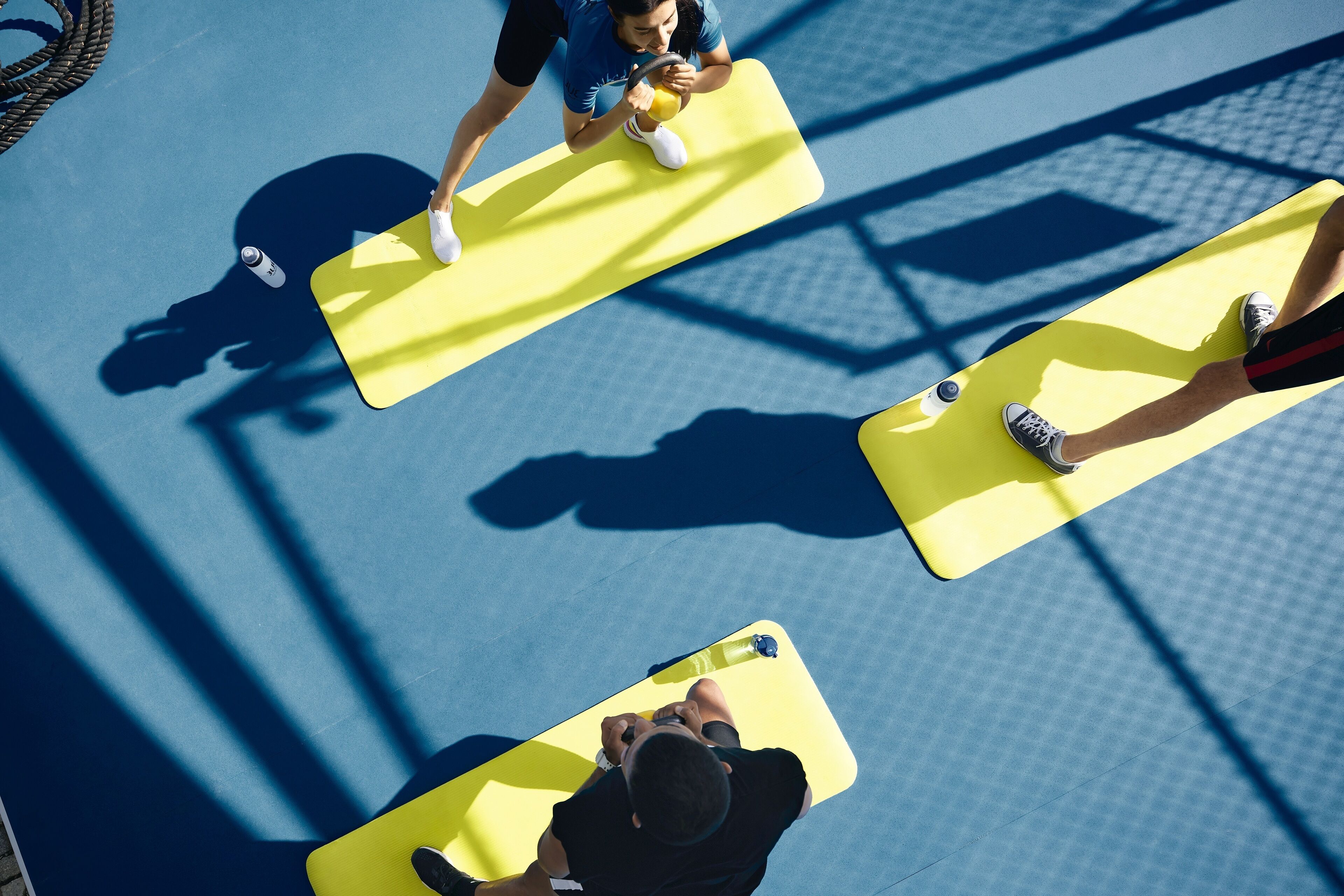 A top-down view of a tennis court with three players on yellow mats.