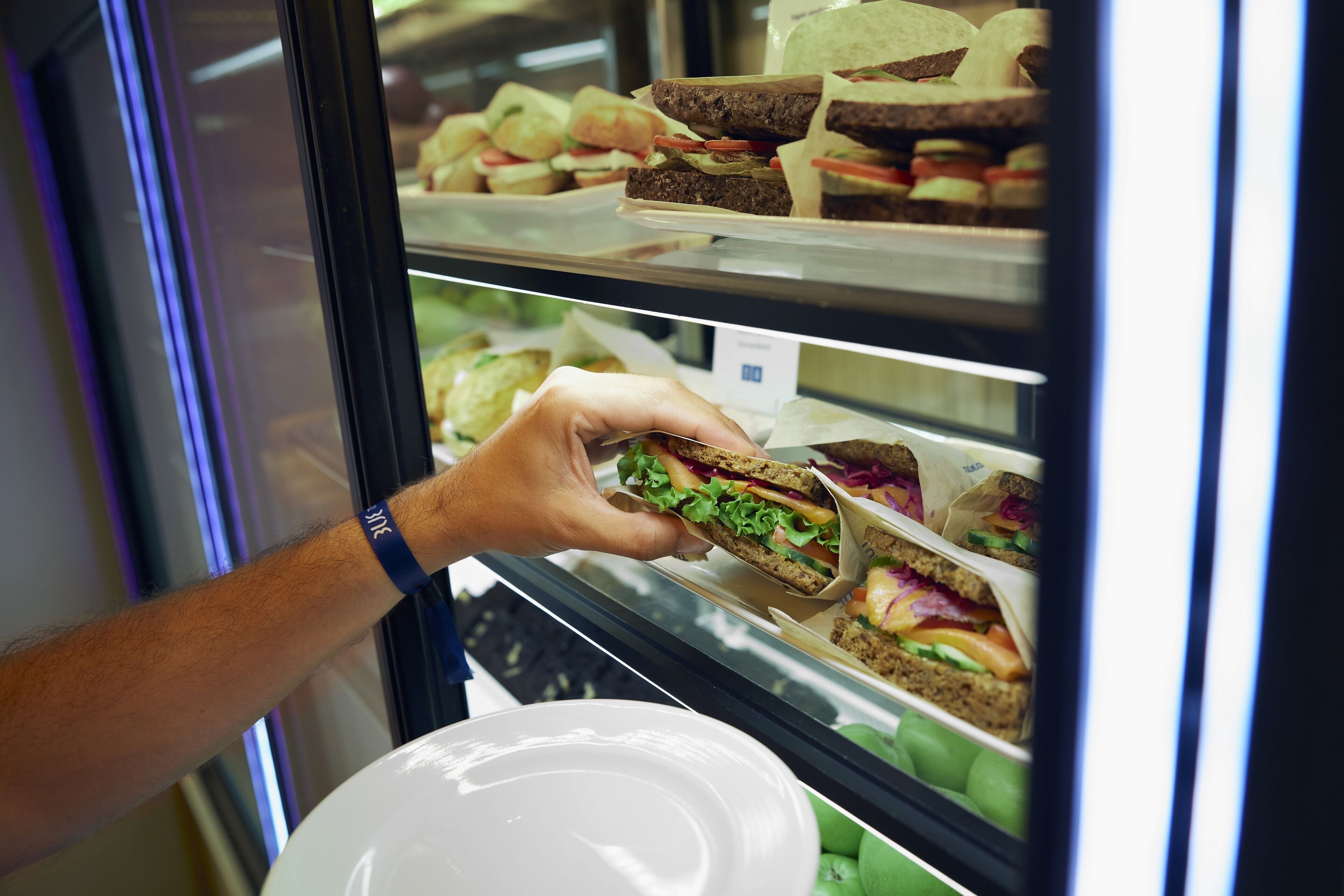 A hand selecting a sandwich from a refrigerated display case in a food service area.
