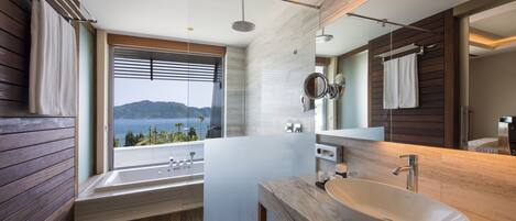A modern bathroom with a large bathtub, a sink, and a mirror. There is a window providing a view of the sea.