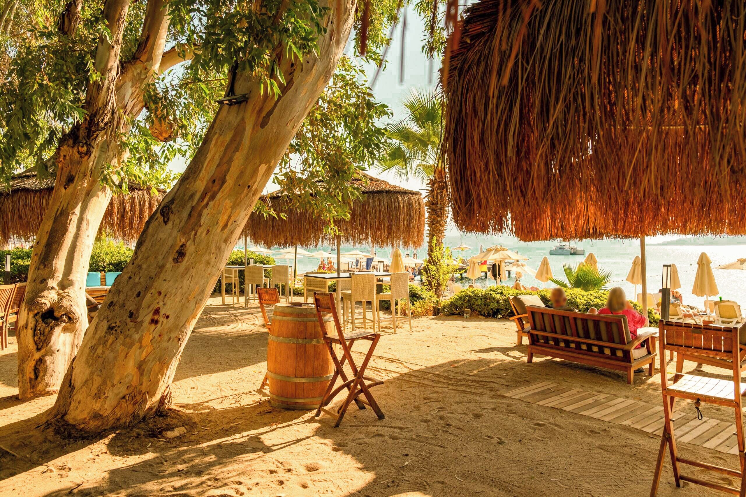 Zona relax in spiaggia con mobili di legno, un ombrellone di paglia e vista sul mare.