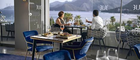 Un coin repas avec une table dressée pour deux personnes, offrant une vue imprenable sur les montagnes.