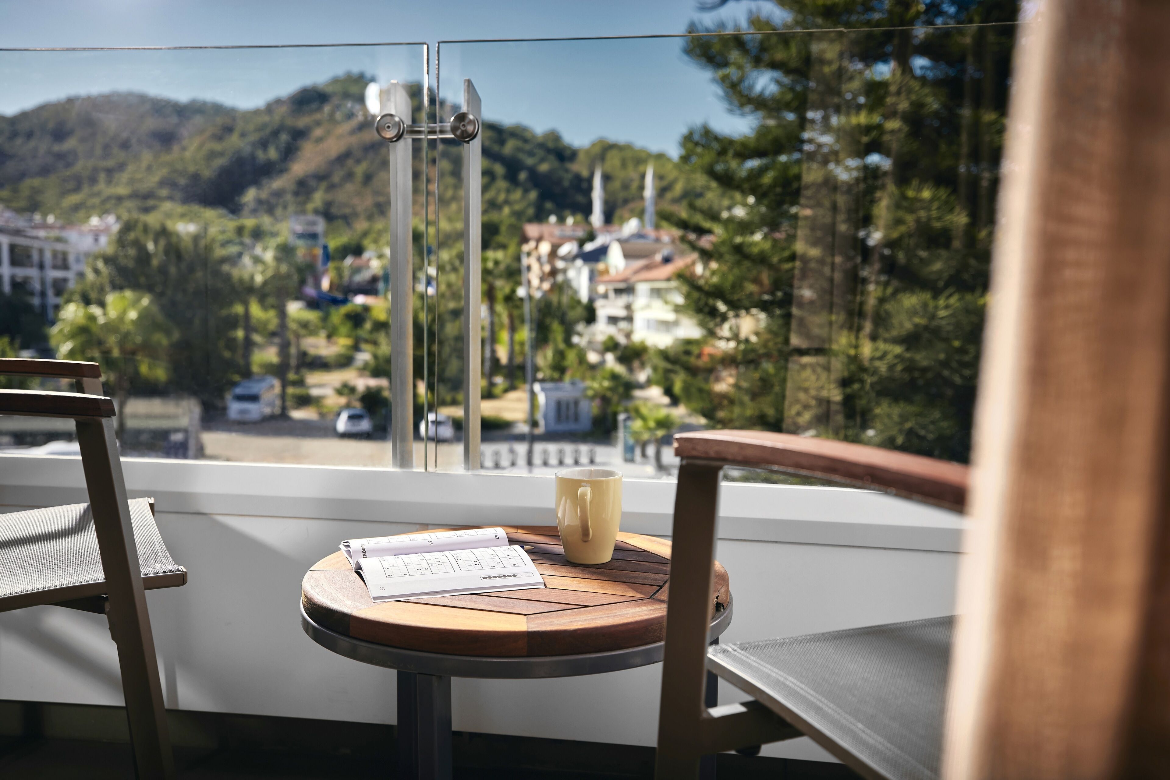 Un balcón con una mesa, sillas y vistas a una colina con edificios.