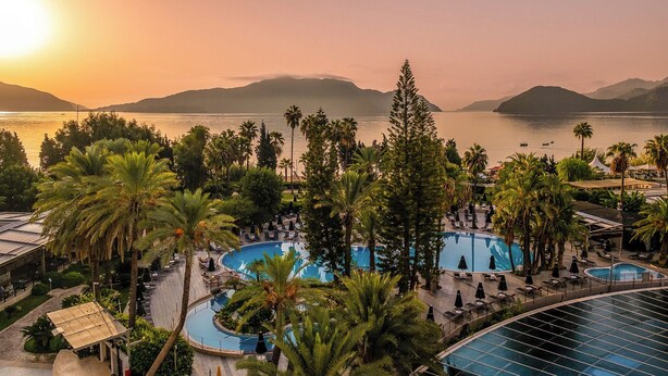A resort with multiple swimming pools, palm trees, and a view of the sea and mountains.