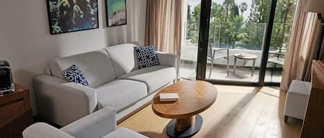 A modern living room with a sofa, a coffee table, and a balcony with a view of trees and a body of water.