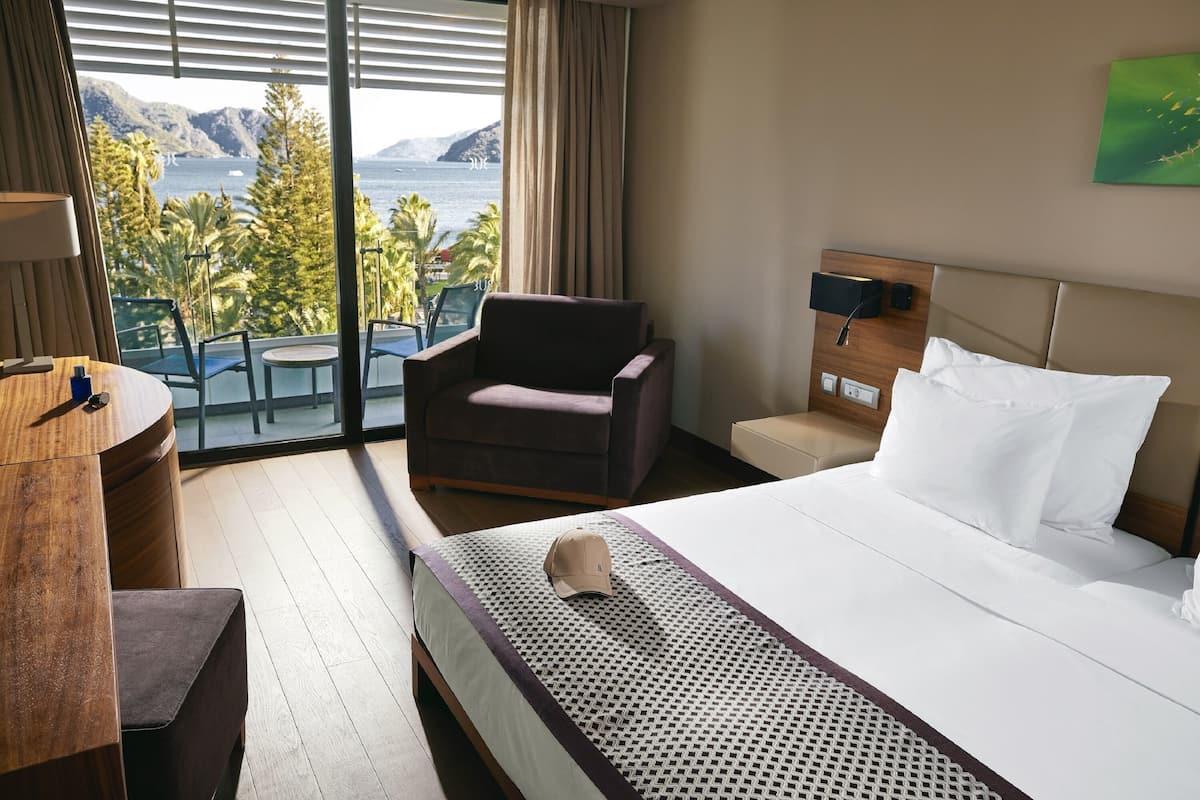 A hotel room with a bed, a chair, a desk, and a view of the sea.