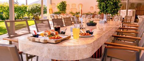 Una larga mesa de comedor con sillas, diferentes alimentos y una bebida.