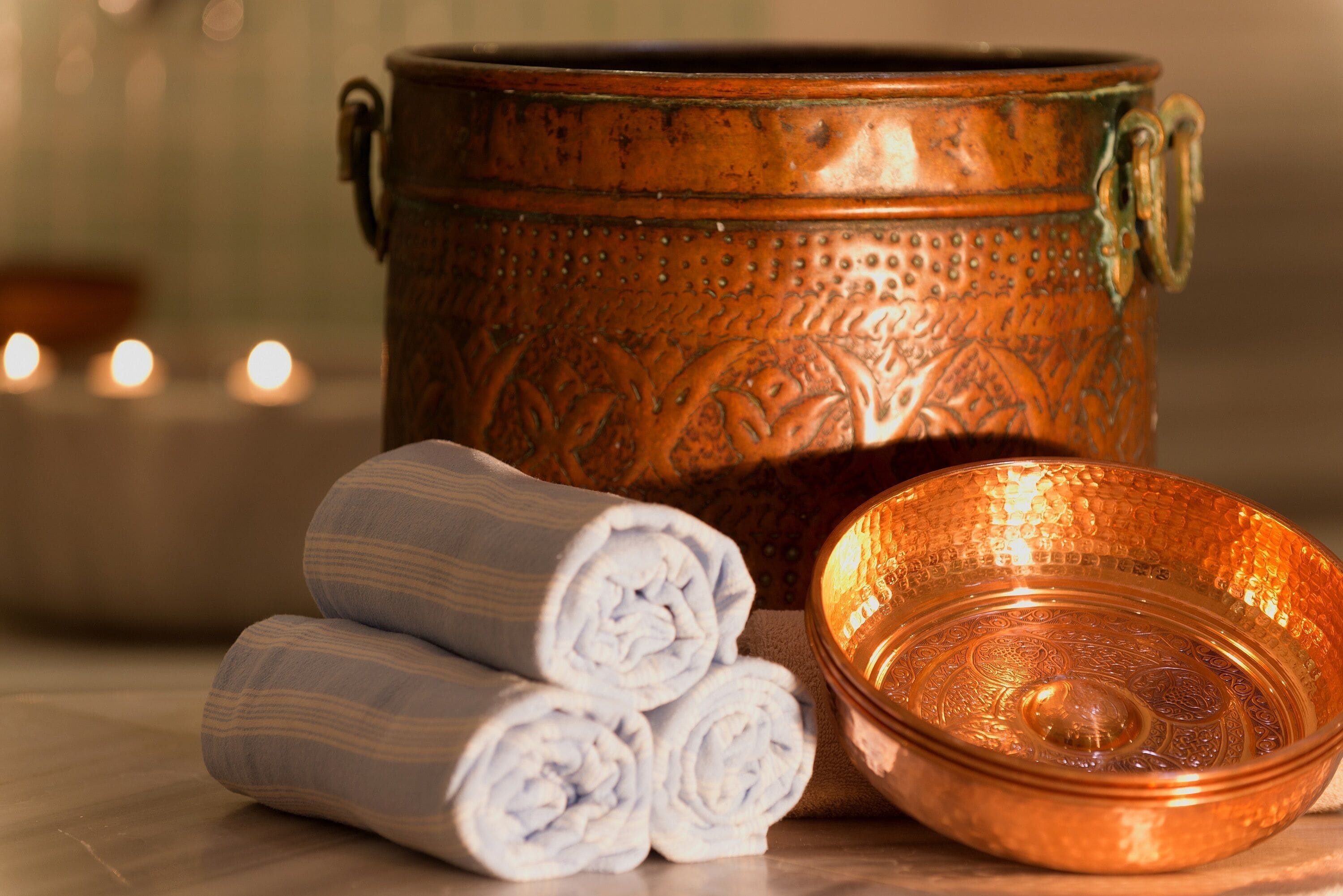 A copper pot, a rolled towel, and a copper bowl on a table.