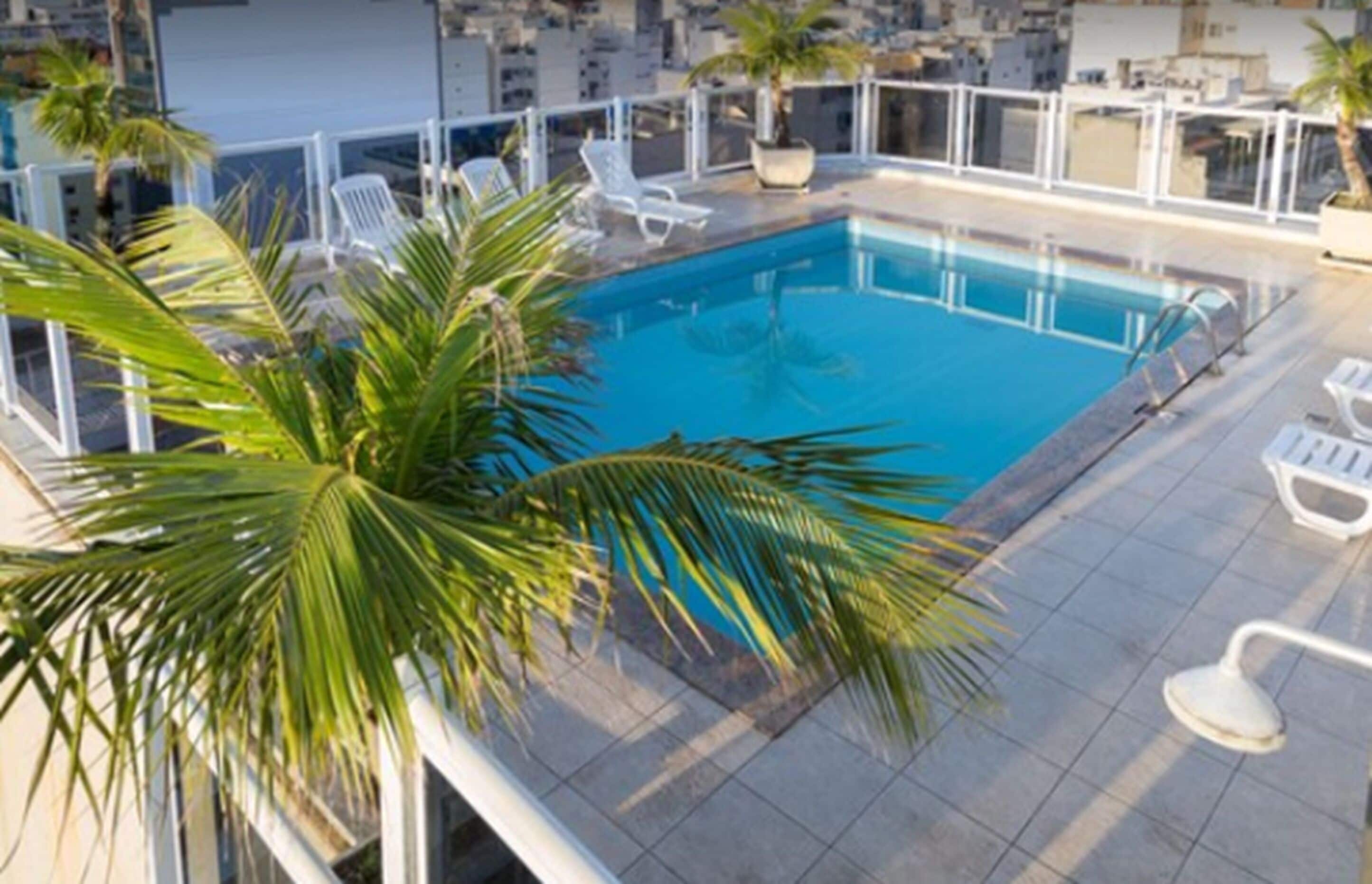 Ein Pool auf dem Dach mit klarem, blauem Wasser, umgeben von weißen Liegestühlen und Palmen.